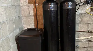 Two water treatment media tanks installed against a stone foundation in a Southwestern PA basement
