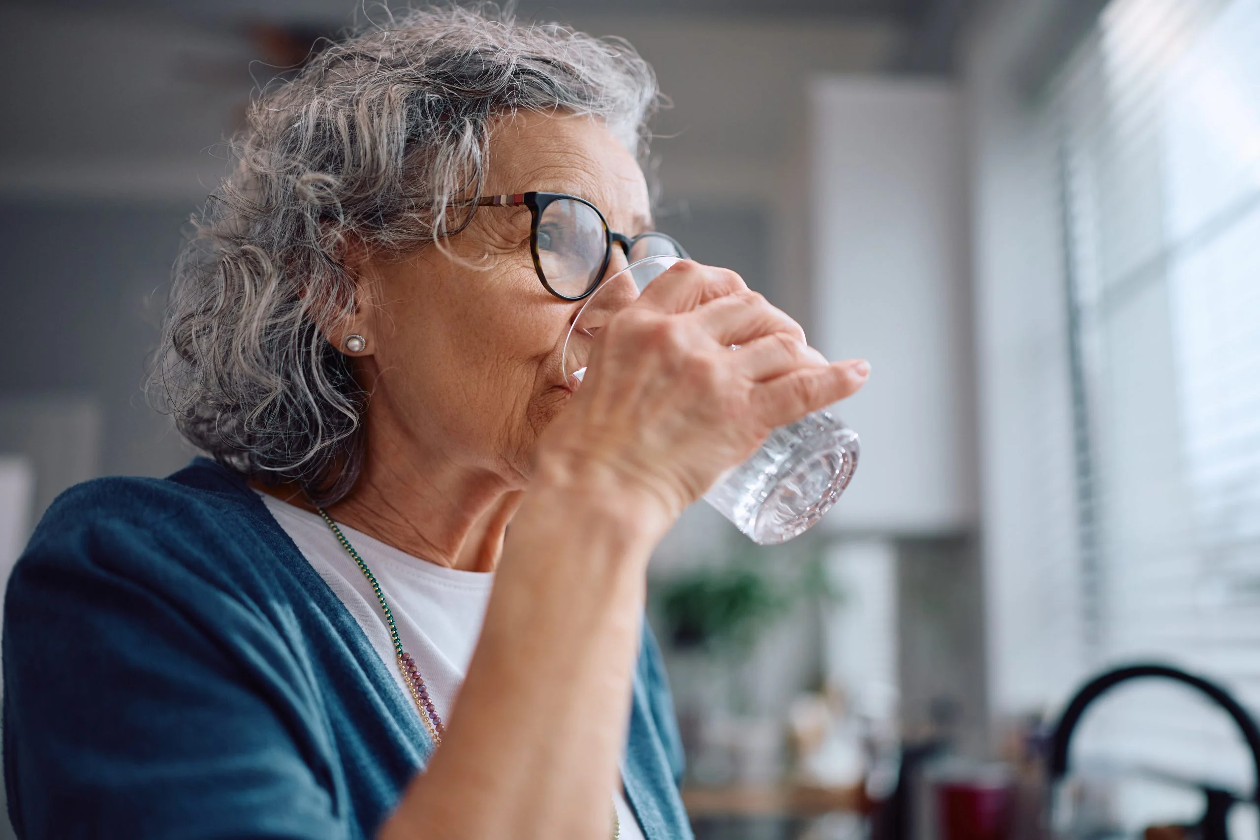 Older homeowner drinking a glass of water in her kitchen