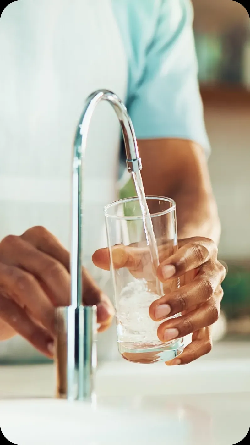 Homeowner filling a glass with fresh, clean drinking water from a kitchen faucet after whole-home water treatment.