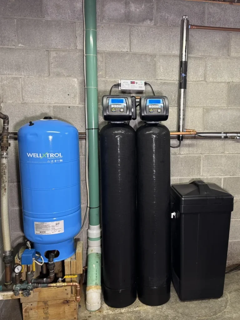 Cesare's private well water treatment install: WellXTrol pressure tank, twin softener and filter tanks on Cesare's control valves, brine tank and a wall-mounted UV disinfection lamp in a block-wall basement