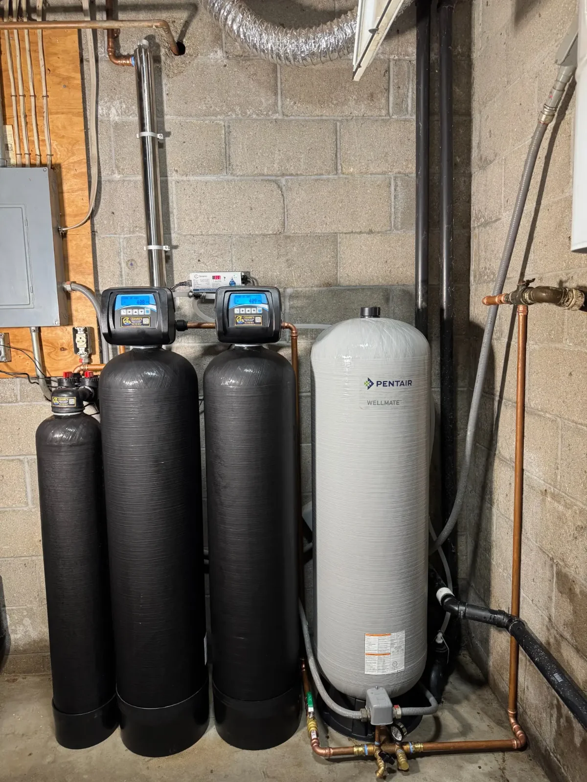 Cesare’s well water treatment installation with three black treatment tanks, a vertical stainless-steel UV chamber and a pressure tank.